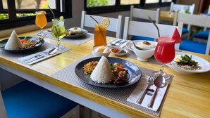 A dining table with various dishes and drinks, including rice, noodles, and a red drink with a watermelon slice. - The Happinezz Hills Hotel Karimunjawa (Karimun Jawa)