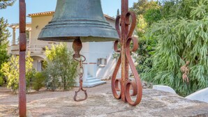 Een grote, verroeste klok bevestigd aan een stenen constructie, met een metalen haak en decoratieve details.