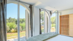 Een slaapkamer met grote, gebogen ramen, een bed met een groene deken en een houten scherm aan de rechterkant.