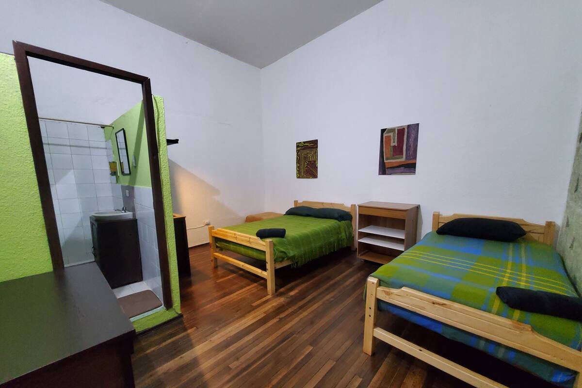 A small, clean room with two wooden beds, a small wooden nightstand, a green wall, and a white door.