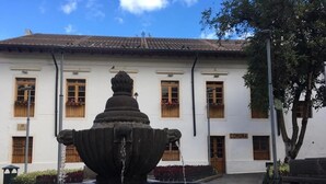 A courtyard with a stone fountain in the foreground and a white building with wooden shutters in the background. - Casa de las Culturas San Marcos (Quito)
