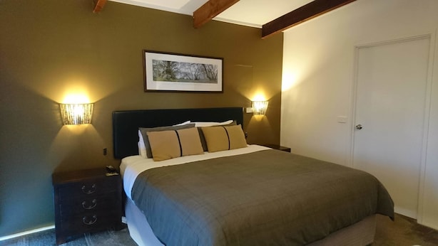 A bedroom with a bed, two bedside lamps, a nightstand, a framed picture on the wall, and a door. - Elm Riverside Accommodation Merrijig (Merrijig)