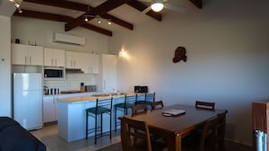 A compact kitchen with white cabinets, a built-in microwave, and a small island with bar stools. - Elm Riverside Accommodation Merrijig (Merrijig)