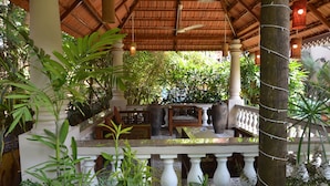 Un espacio al aire libre techado, con techo de madera, columnas blancas y barandilla.
