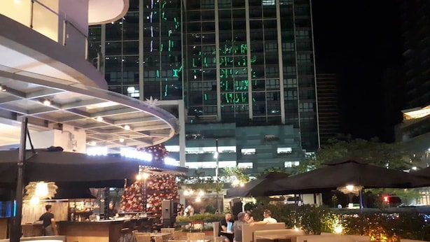 An outdoor dining area with tables and chairs, a bar, and a large building with illuminated windows in the background. - Uptown BGC near St. Luke's (Taguig)