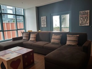 A living room with a large window, a sofa set, and a wooden play table with dice.