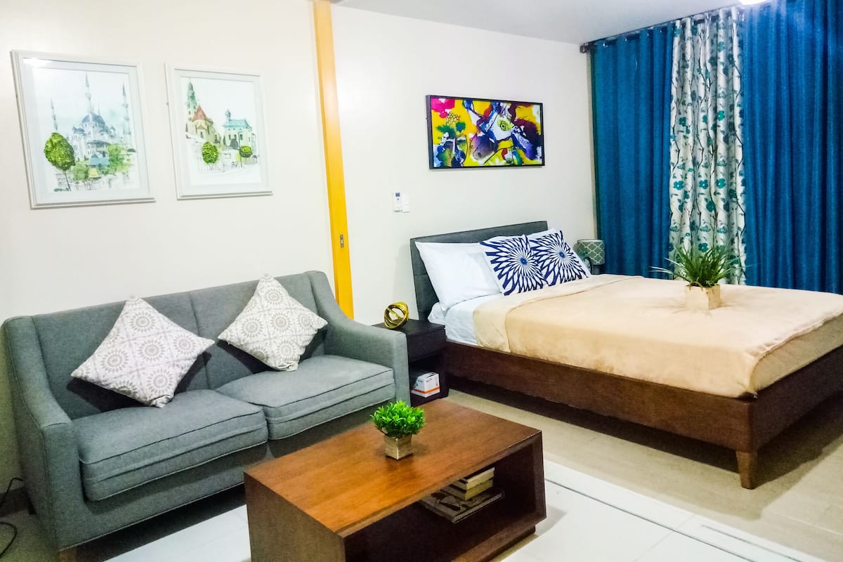 A modern bedroom with a bed, a grey sofa, a coffee table, and two framed pictures on the wall.