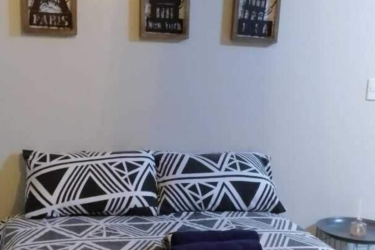 A bed with a geometric patterned bedspread, two wall-mounted artworks depicting famous landmarks, and a small round table with a candle.