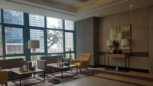 A modern hotel lobby with large windows, a sofa, armchairs, a coffee table, and a side table with lamps. - Uptown BGC near St. Luke's (Taguig)