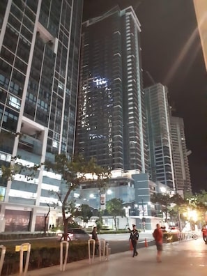 A nighttime view of a modern urban area with high-rise buildings, a pedestrian walkway, and a few people walking.