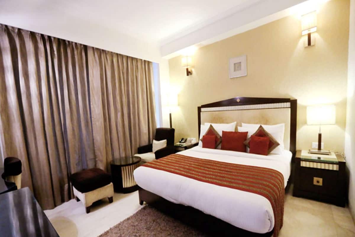 A hotel room with a large bed, a desk, a chair, a nightstand, and a lamp.
