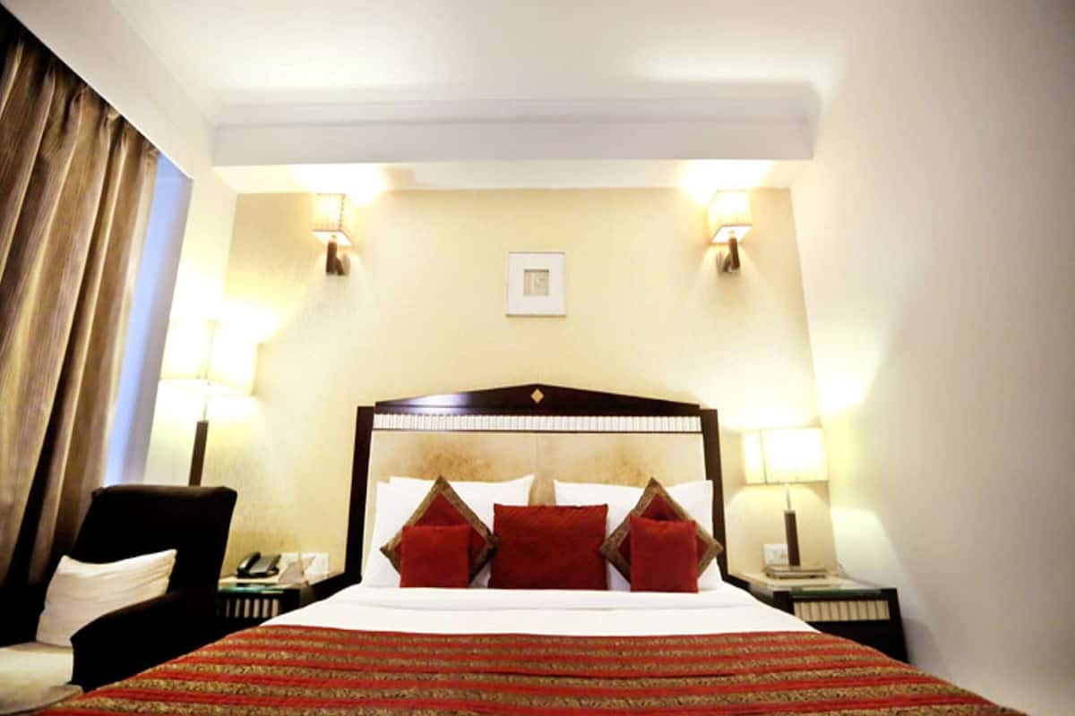 A hotel room with a large bed, two bedside lamps, a chair, and a nightstand with a phone.