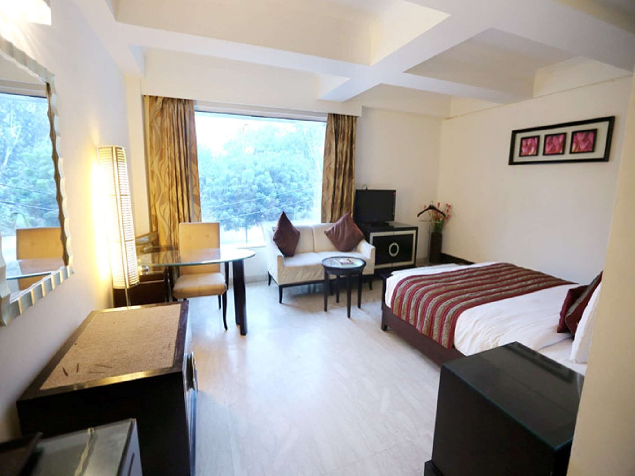 A hotel room with a bed, a desk, a chair, a TV, and a window with curtains.