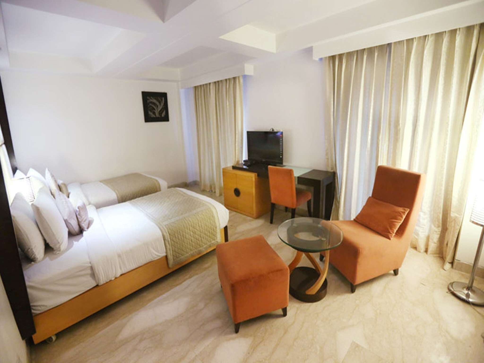 A hotel room with a bed, two armchairs, a small table, a desk with a TV, and curtains.