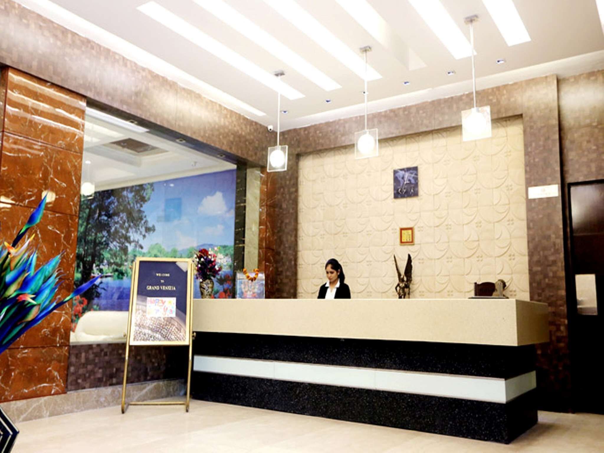 A hotel reception area with a marble reception desk, a receptionist, and a welcome sign.