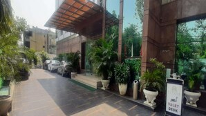 Entrada de hotel con un vestíbulo techado, plantas en macetas y señalización de servicio de botones.