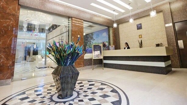 Zona de recepción de hotel con diseño moderno, que incluye un mostrador de mármol, un jarrón grande con plantas decorativas y un suelo con motivo circular.