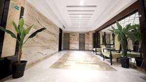 Un vestíbulo de hotel con suelo de mármol, plantas en macetas y una zona de estar con sillas.