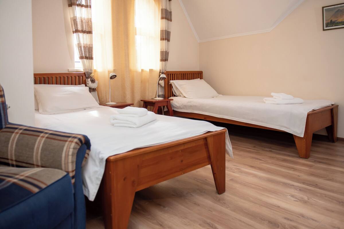 Una stanza con due letti in legno, un divano blu, un comodino in legno e una finestra con tende.