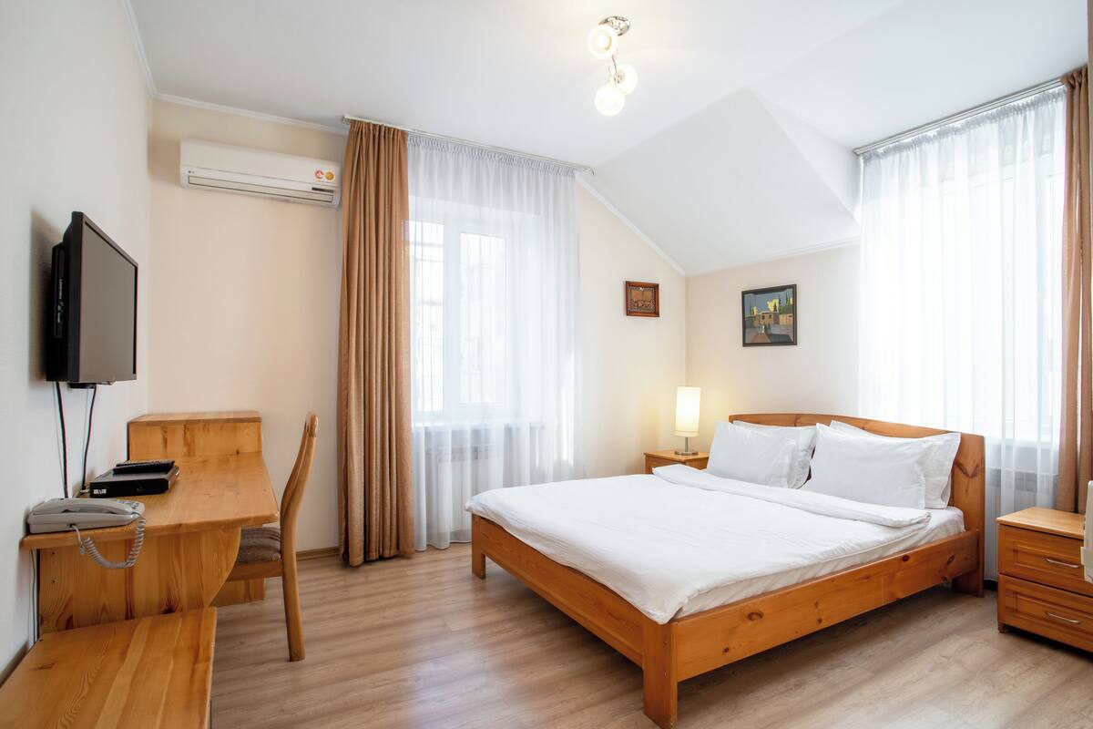 Camera da letto con un letto in legno, una scrivania, una sedia, un televisore e un comodino con una lampada.