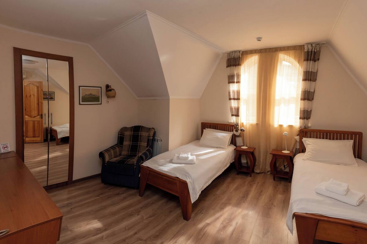 Camera da letto con due letti, una scrivania in legno, una sedia, uno specchio e una finestra con tende.