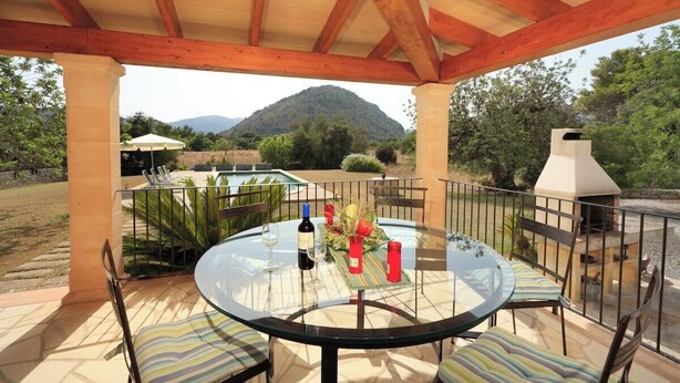 Une terrasse extérieure avec une table ronde en verre, des coussins à rayures et une vue sur une montagne.