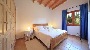 Une chambre avec un lit en bois, deux tables de chevet avec des lampes, une fenêtre avec des rideaux et une vue sur la verdure à l’extérieur.