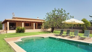 Une maison avec une piscine, une terrasse avec des chaises et un grand parasol.