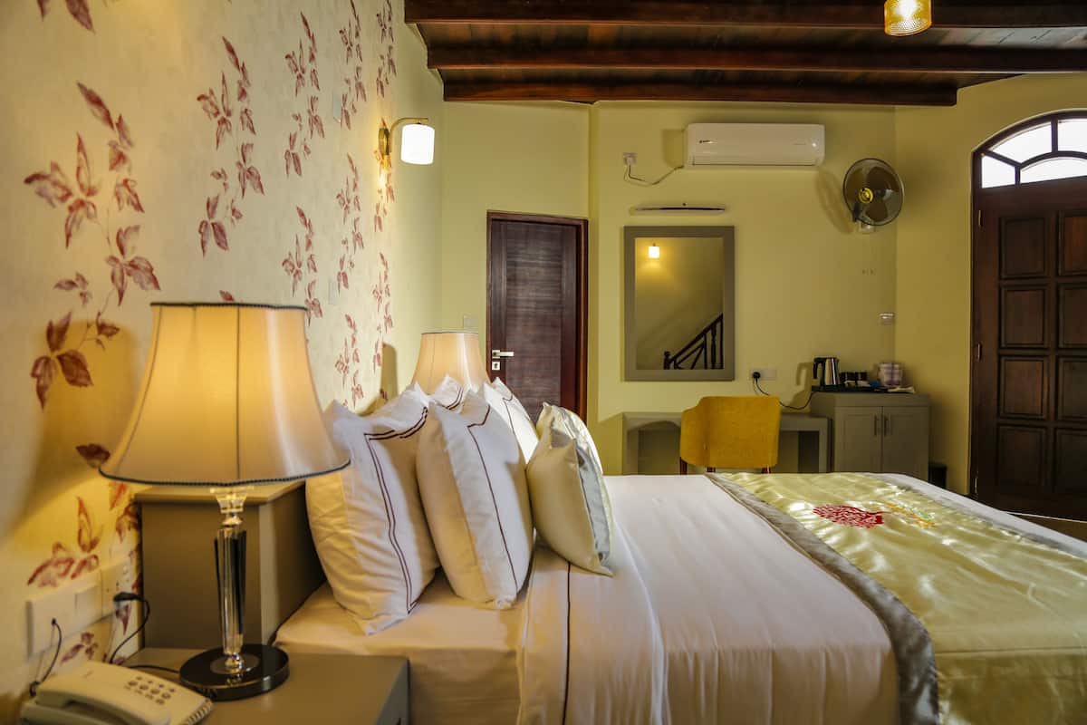 A hotel room with a bed, bedside lamps, a telephone, a mirror, and a wardrobe.
