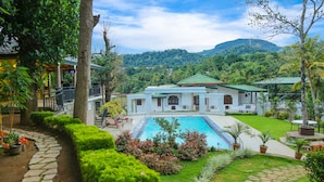 Een resort met een zwembad, weelderige begroeiing en uitzicht op de bergen.