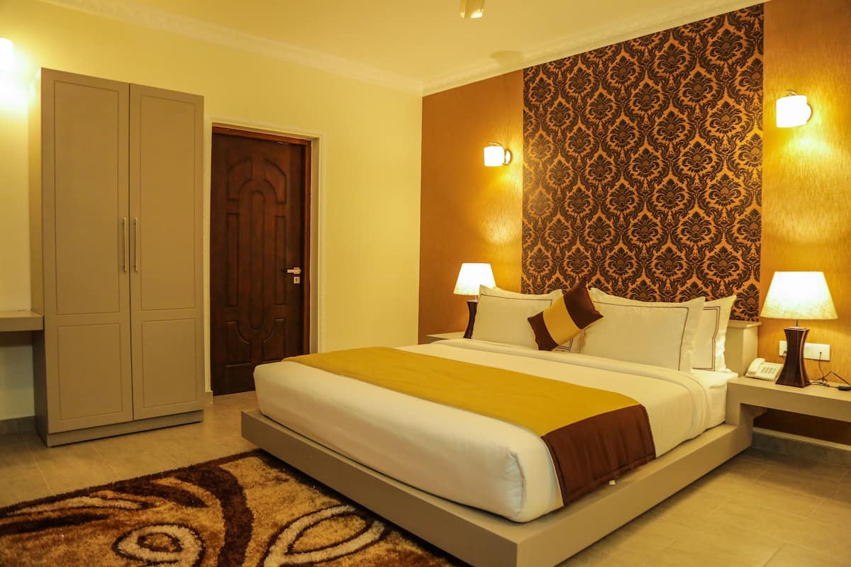 A hotel room with a large bed, two bedside lamps, a wooden wardrobe, and patterned wallpaper.