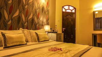 A hotel room with a bed, pillows, a nightstand, a lamp, a wooden door, and a wall with a leaf pattern.