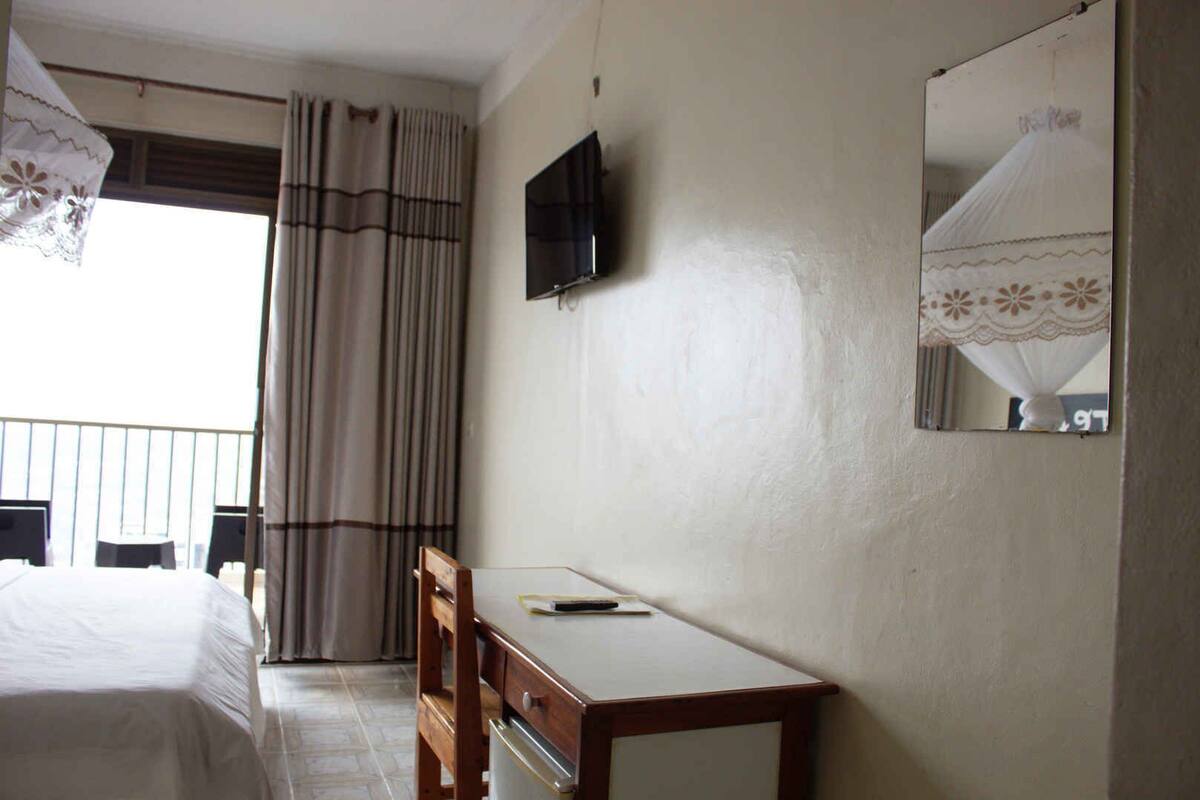 Une chambre d’hôtel avec un lit, un bureau, une télévision et une fenêtre avec des rideaux.