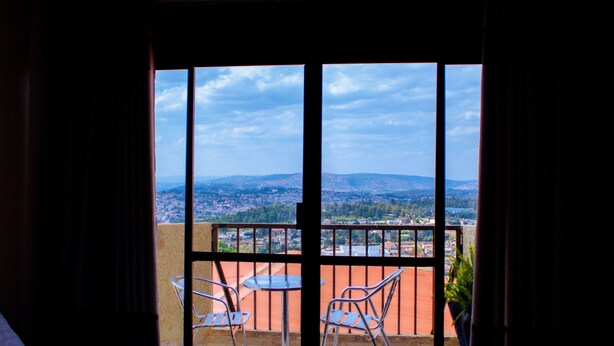 Un balcón con dos sillas de metal y una mesa, con vista a un paisaje urbano y colinas al fondo.