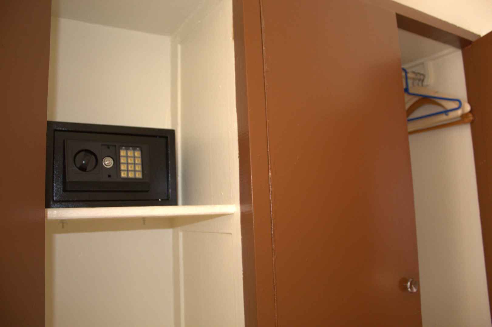 Ein Zimmer mit wei ßer Wand, einer braunen Tür und einem Regal mit einem schwarzen elektronischen Gerät.