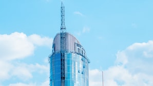 Un edificio moderno con una estructura cilíndrica y una aguja, rodeado de otros edificios.