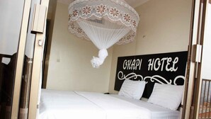 Una cama con ropa de cama blanca, un dosel con motivos florales y un letrero que dice "OKAPI HOTEL".