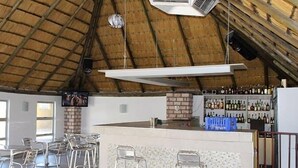 A bar area with metal stools, a brick counter, and a ceiling with wooden beams and air conditioning units. - Ekamuti Town lodge (Ondangwa)