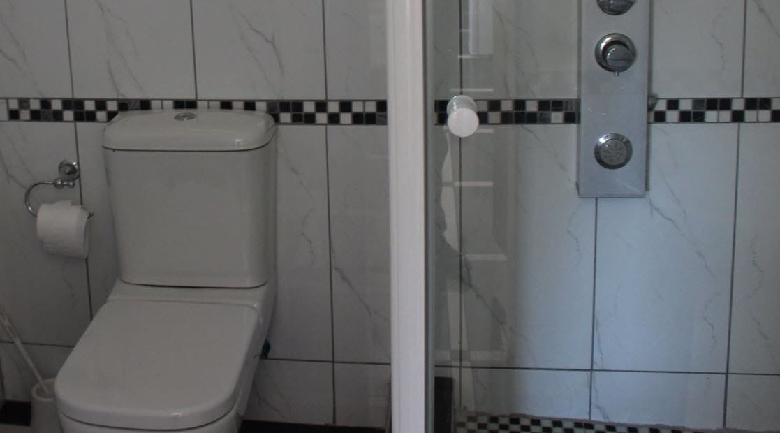 A bathroom with a toilet, a shower, and a tiled wall with a checkered pattern.