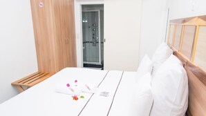 Siististi pedattu sänky valkoisilla lakanoiden kanssa ja puinen pääty, puinen vaatekaappi ja lasinen suihkuovi.