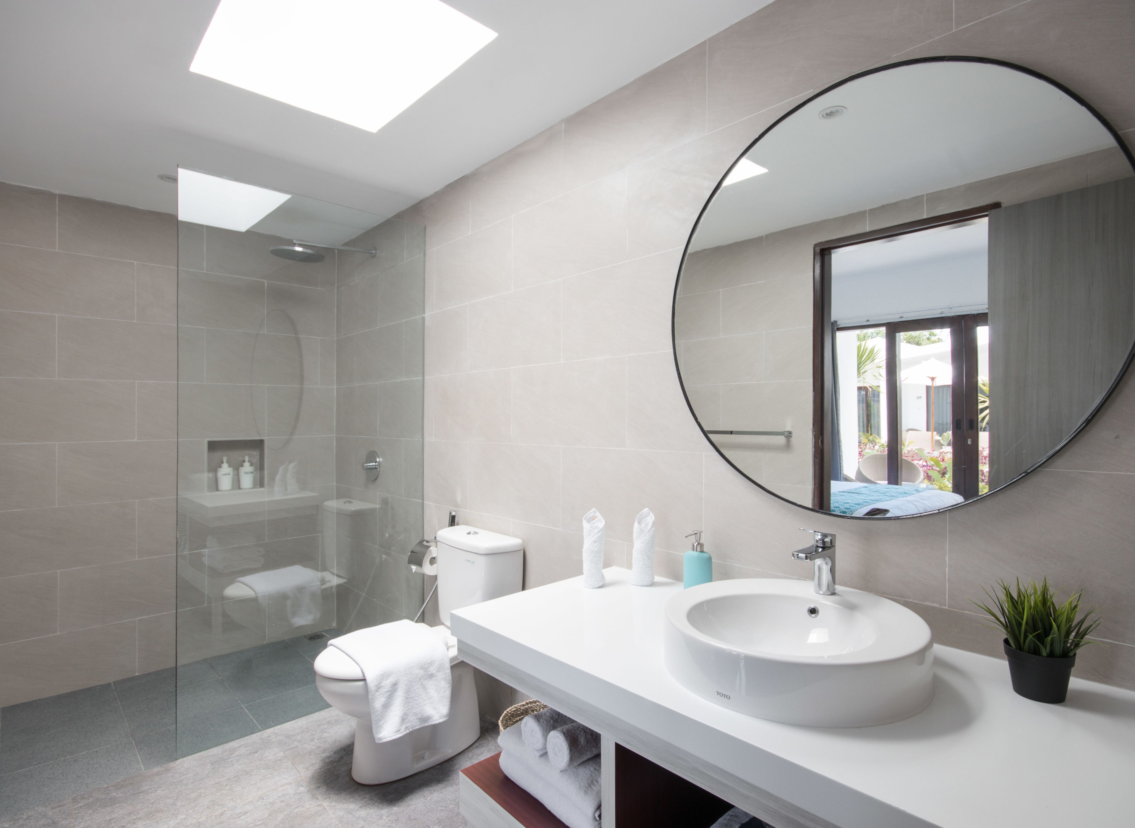 Un baño moderno con ducha envuelta en vidrio, inodoro, lavabo con espejo y una pequeña planta en maceta.
