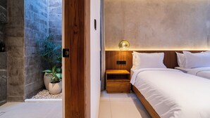 Un dormitorio moderno con pared de piedra, una mesita de noche de madera y una cama con ropa de cama blanca.