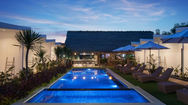 Un área junto a la piscina con sillones, sombrillas y un bar.