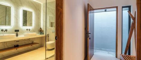 A modern bathroom with two sinks, a toilet, and a glass shower enclosure.