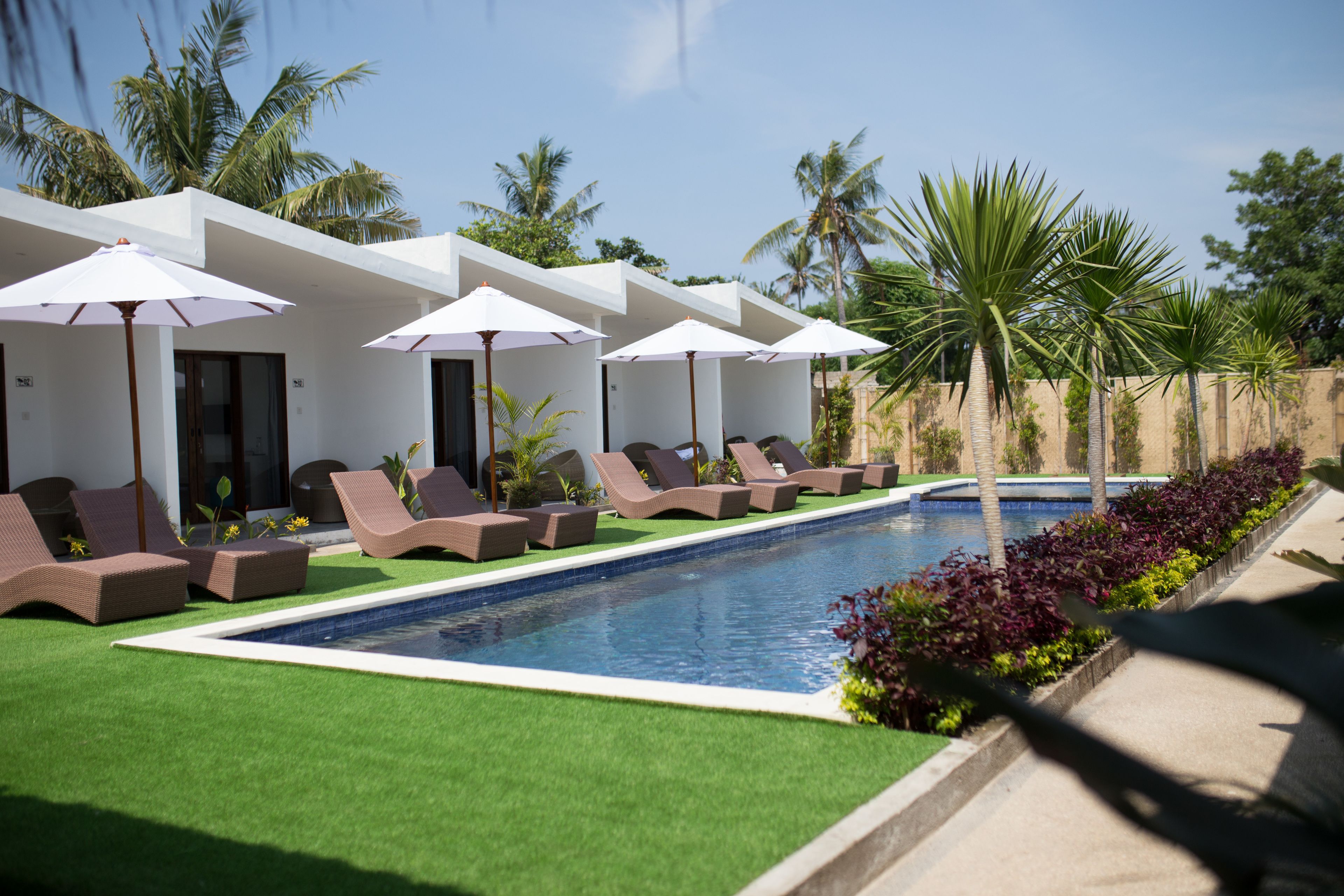 A pool area with lounge chairs and umbrellas, surrounded by palm trees and a clear sky.
