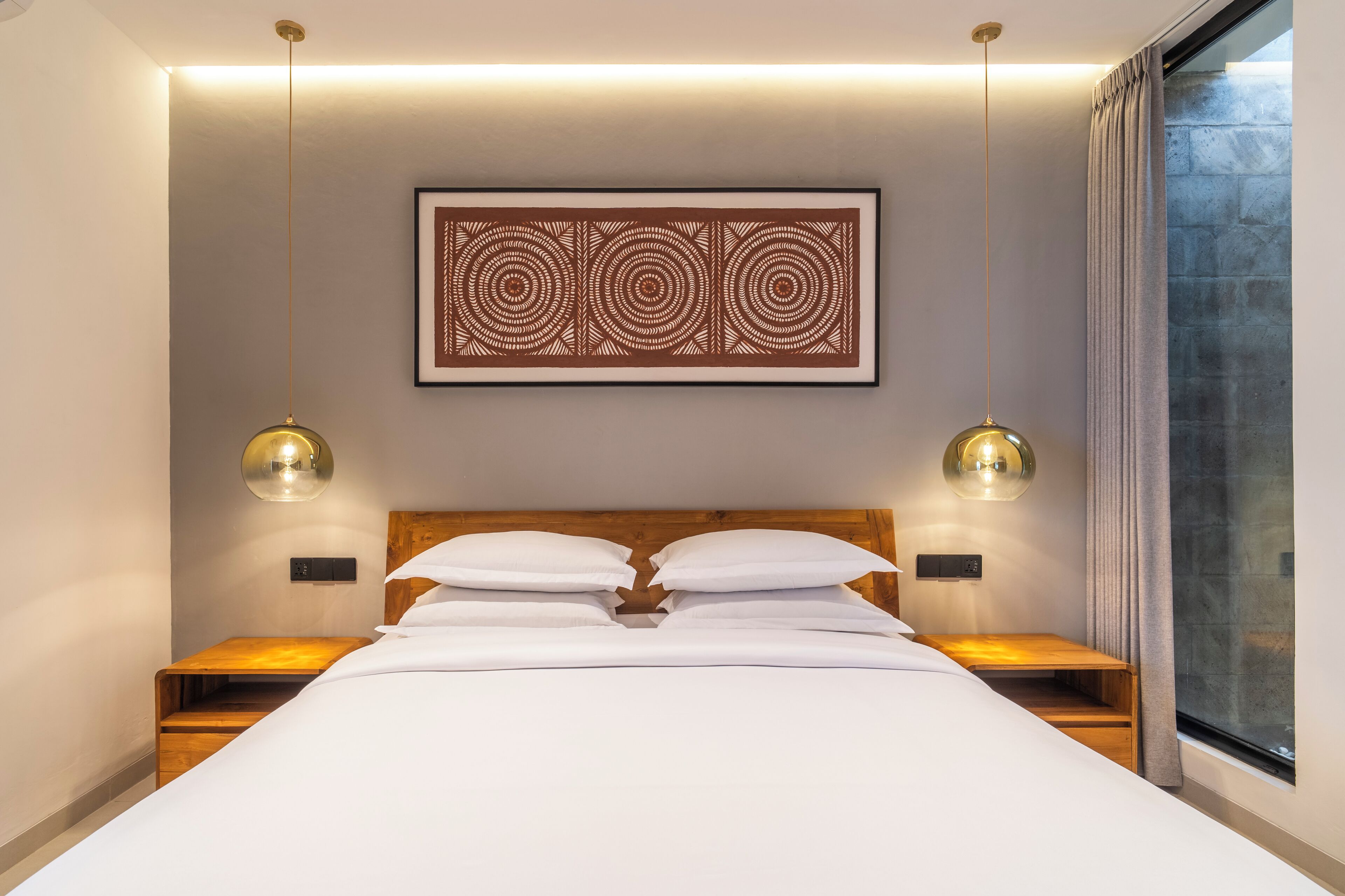 A modern hotel room with a large bed, two bedside tables, a wall-mounted artwork, and two pendant lights.