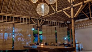 Espacio interior con techo alto, estructura de bambú y lámparas esféricas colgantes. Mesas y bancos dispuestos para sentarse.