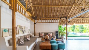 Amplia sala de estar con techo de bambú, un conjunto de sofás, una mesa de centro y vistas al jardín.