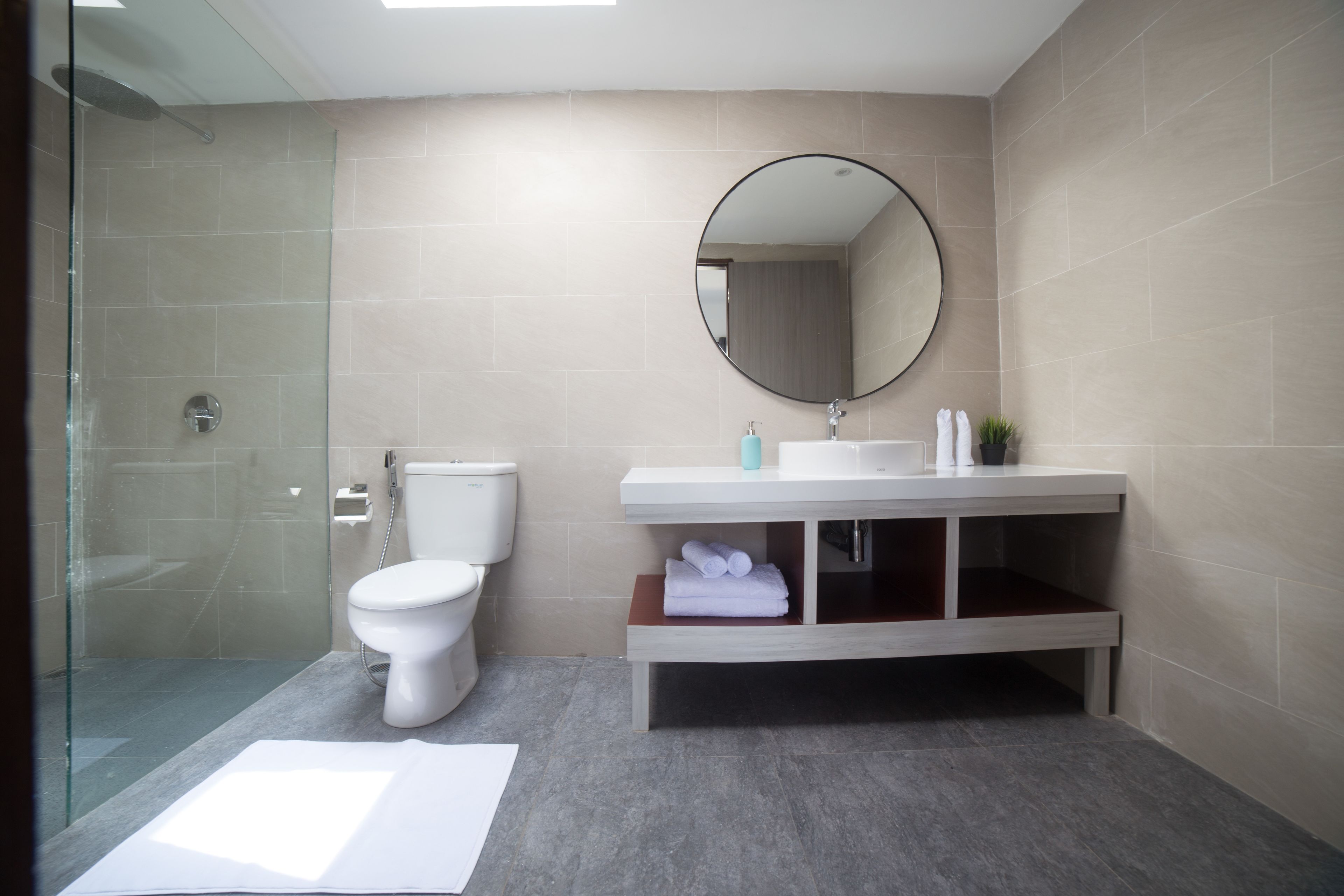 Une salle de bain moderne avec une douche à parois de verre, des toilettes, un lavabo avec un miroir et des serviettes soigneusement pliées, rangées sur une étagère.