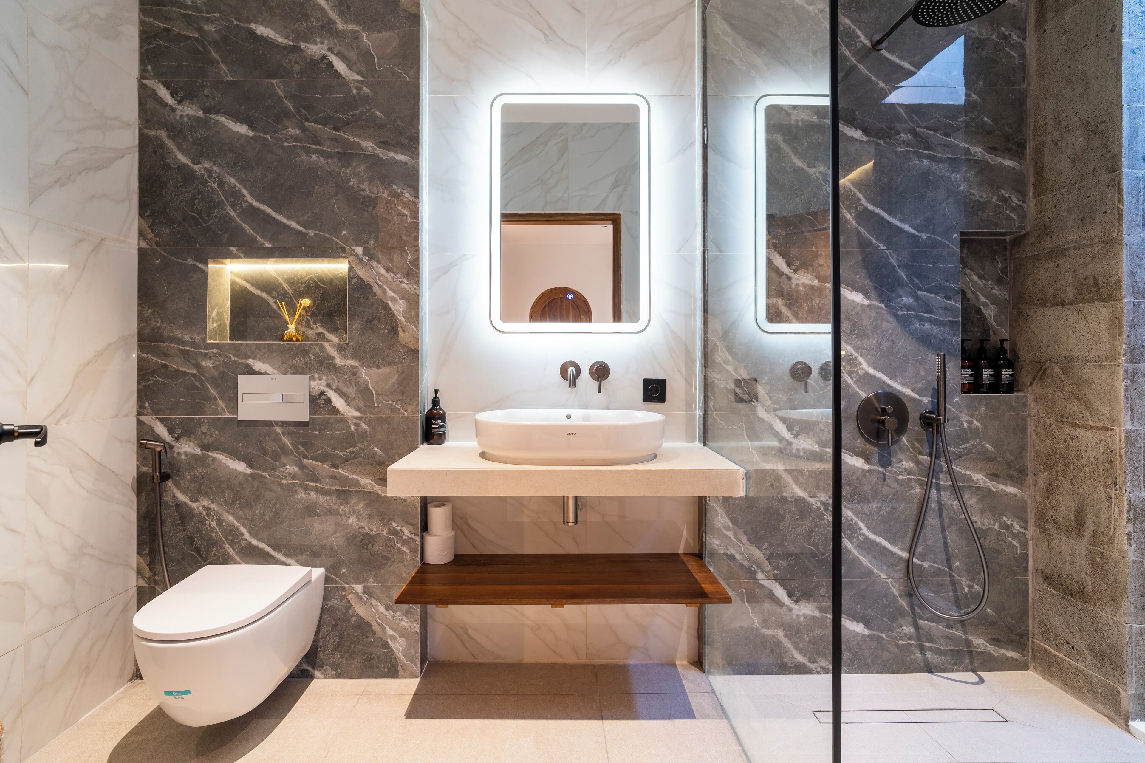 Un baño moderno con resguardo de mármol, un lavabo redondo, un espejo y una zona de ducha.